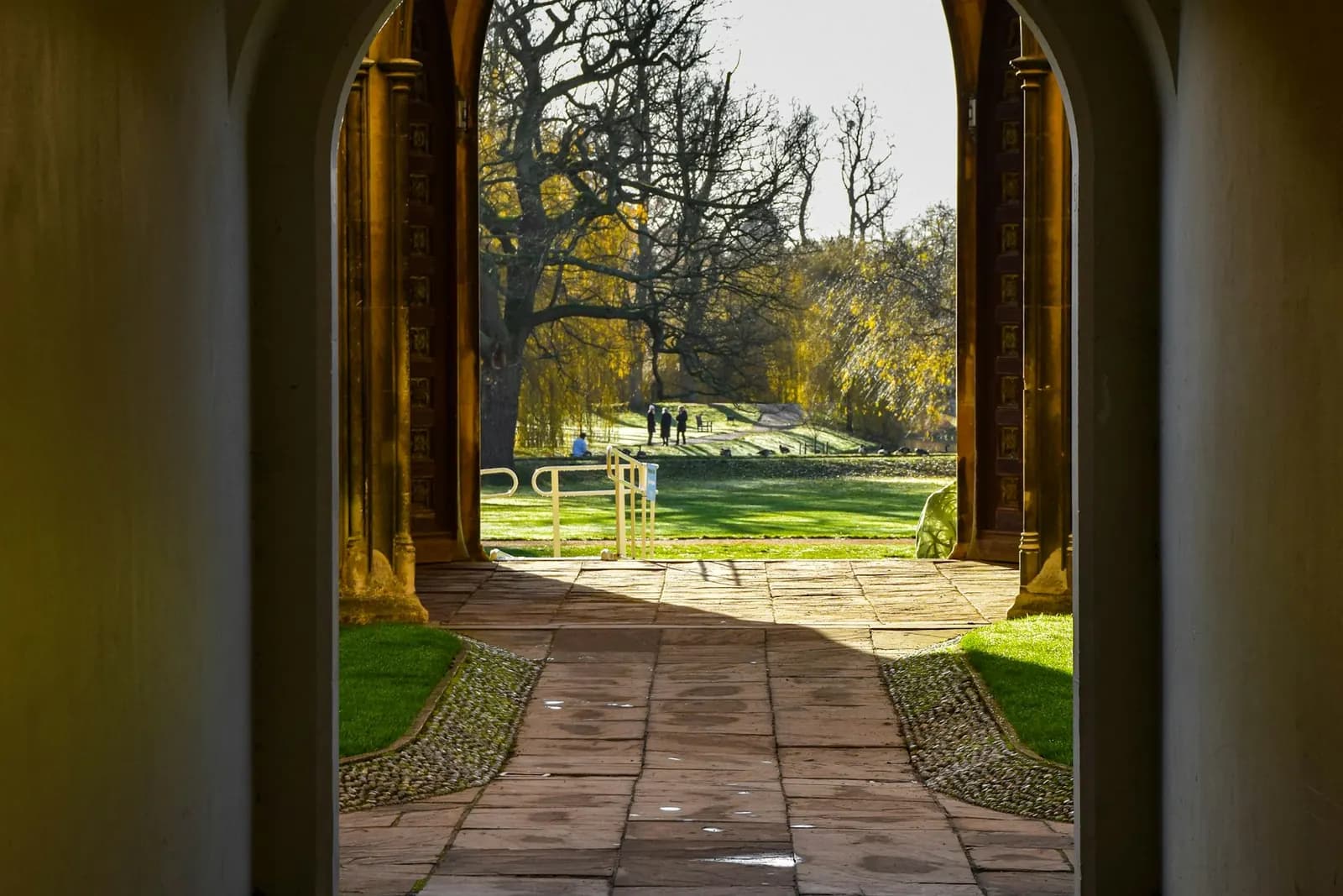Lối đi bộ và khu vườn đầy nắng nhìn qua vòm đá ở Cambridge, Anh